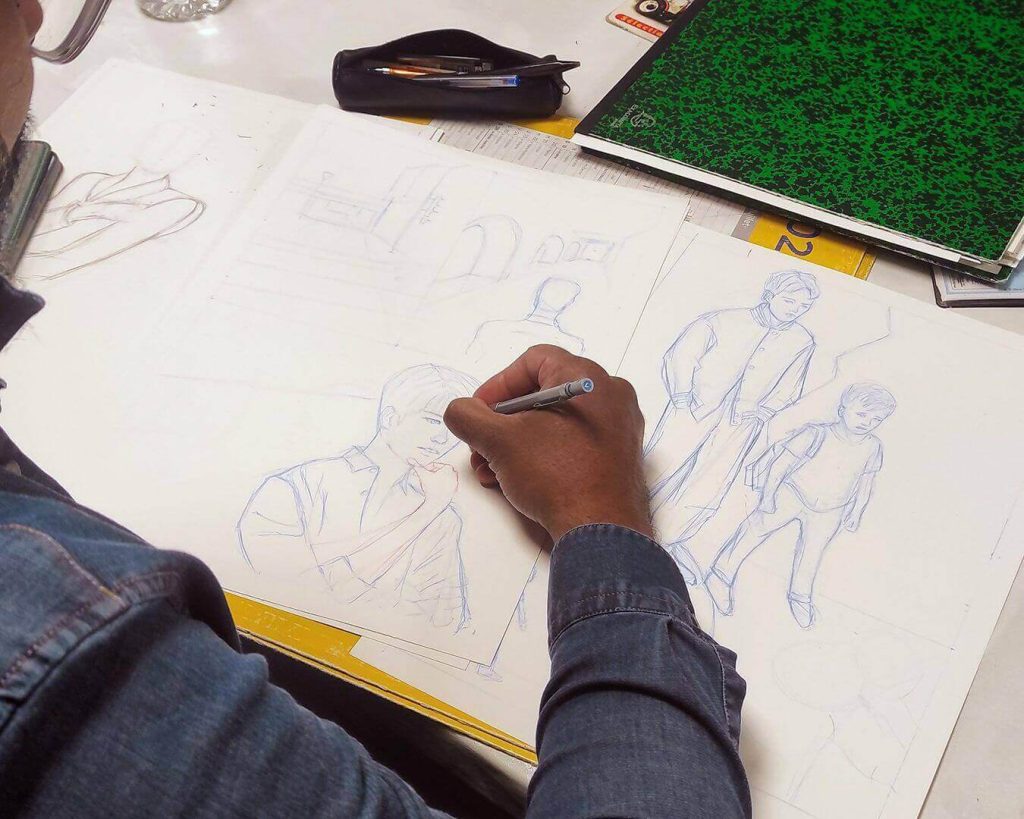 Un adulte en cours de BD au Cardo à Nantes dessine une recherche de personnages à la mine bleue pour une planche de bande dessinée.